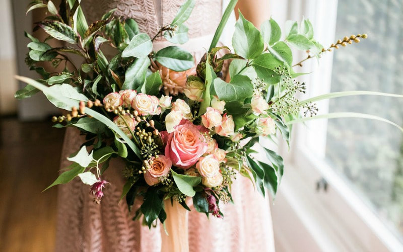 Frontfacing bridal bouquet in peach & coral shaeds with foliage