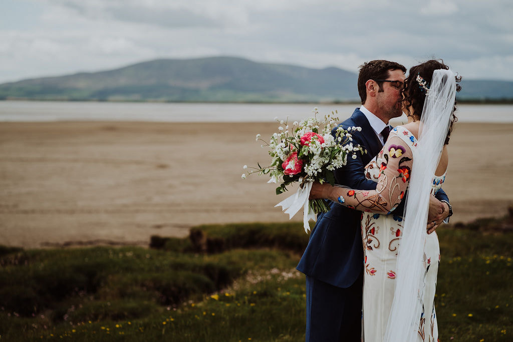 Wedding couple on Solway coast with bouquet of coral Peonies plus white flowers, wedding florist Dumfries www.gallowayflowers.co.uk. Photo credit Amy Sampson Photography