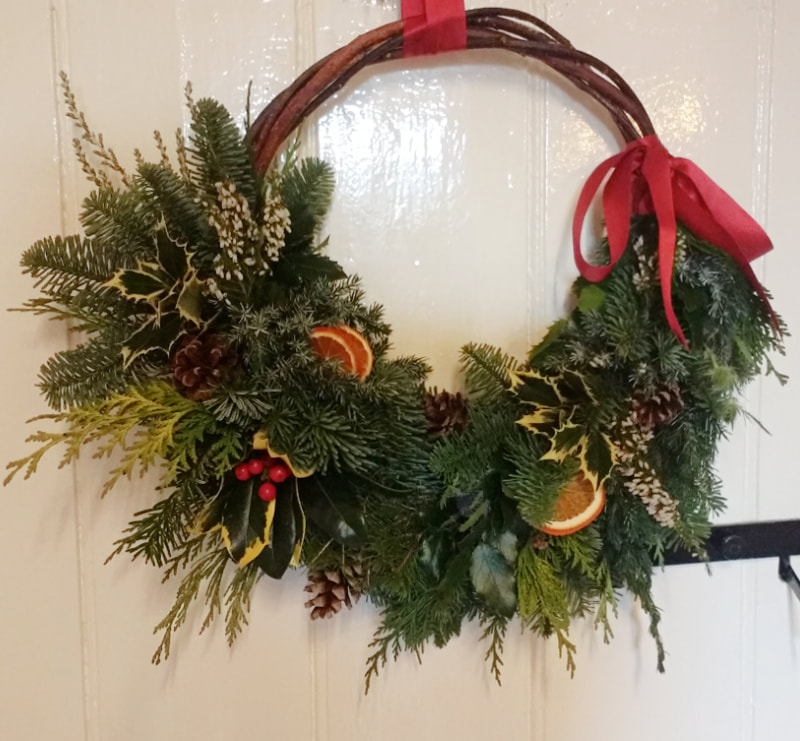 Contemporary Willow Hoop Wreath for Christmas, trimmed with mixed Conifers, Hollies, Cones, Heather, Orange slices & a red Ribbon bow. Copyright www.GallowayFlowers.co.uk